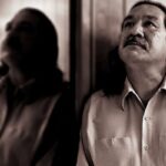 Photo of a Native American man, Leonard Peltier, standing with his side against a mirror, gazing upwards.